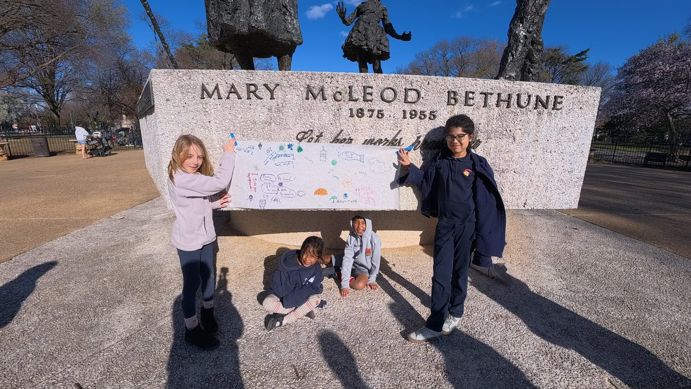 Kids hold up their drawn banner of wishes against the Bethune memorial