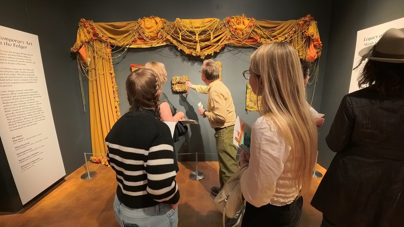Participants look closely at a beaded, draped textile artwork at the Folger