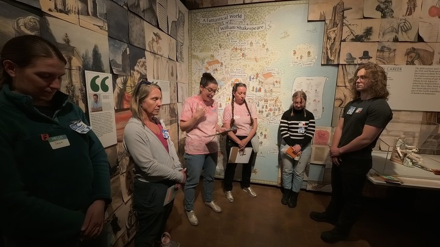 Participants stand with eyes closed in a Folger exhibit gallery as a facilitator reads from a clipboard