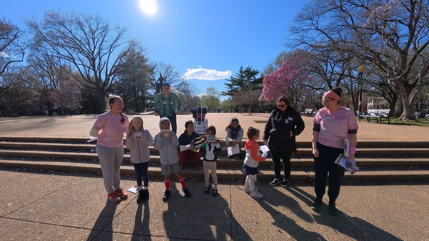 Kids, their adults and two facilitators gather on the steps of Lincoln Park in the spring sun